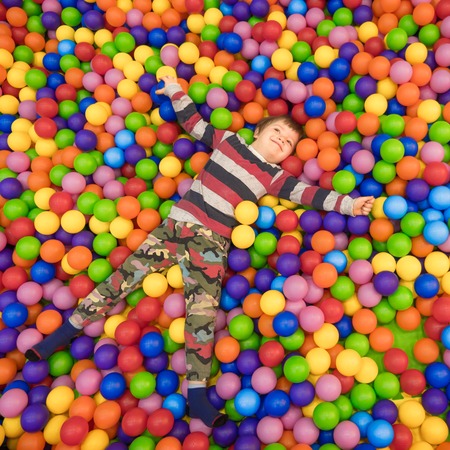 Little boy playing in the pool with plastic balls in the nursery. The kid is swimming. Close-up, real time, artificial light, indoors. Mental health concept. Montessori concept. Happiness concept.の写真素材