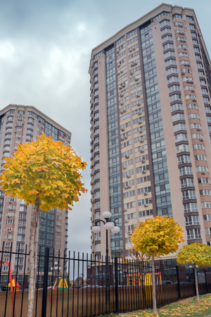 Modern apartment building with a neat adjoining territory and a luscious yellow trees. Residential apartment building on the background of the autumn. Skyscraper with playground territory.の写真素材