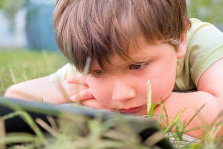 Child with ipad on green grass. Portrait of boy with tablet. Eye problems caused by using tablets too much. Health care concept. Boy with tablet in the park. Summer holidays Alternative educationの写真素材