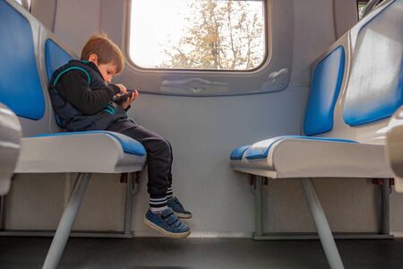 Boy with mobile phone sitting in train. Children and technologies. Young boy playing game on phone while sitting in train. Quality of internet connection. Young traveler travels with electronic mapの写真素材