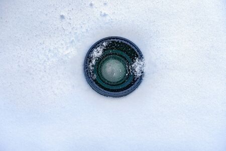Espionage background. Hidden camera lens in the snow. Black lens of the secret camera is hidden in the snow. Copy spaceの写真素材