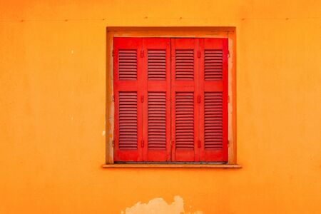 Red shutters on yellow wall background. Building exterior of yellow wall and red shutters. Design in building architecture. Closed shutters on window. View from outside.の写真素材