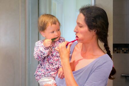 Baby on mothers hands brushing the teeth with mother. Mother and daughter brush the teeth in bathroom. First teeth. Dentistry concept. Mother with child brushing the teeth.の写真素材