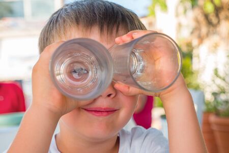 Boy looking through two glasses. Smiling boy. Funny kid joking. Summer vacation.の写真素材