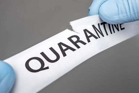 The end of Coronavirus COVID 19 Pandemic. Back to normal life. Hands in medical gloves tearing paper with quarantine written on it. Quarantine is over. Restoration of lifeの写真素材