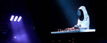 dj mixing music at a party. DJ in stylish protective wearing. Concert during quarantine. Nightlife concept. Disco club with dj and club lights on background. Party with dj in astronaut suitの写真素材