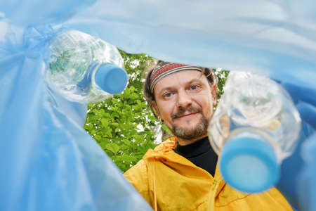 Volunteer collecting litter picking up trash plastic bottle in garbage bag. Picking up garbage...