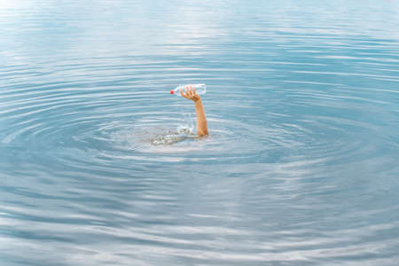 Raised arm holding bottle plastic garbage beach pollution ocean plastic waste ocean trash sea waste. Emerging from water plastic bottle raised hand trash beach. Motivation concept hand trash clean upの写真素材