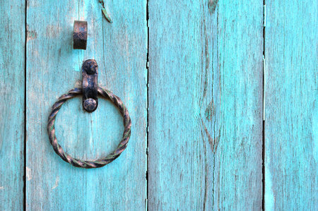 Old textured turquoise wooden door with aged metal door handle in the form of ring. Architectural...