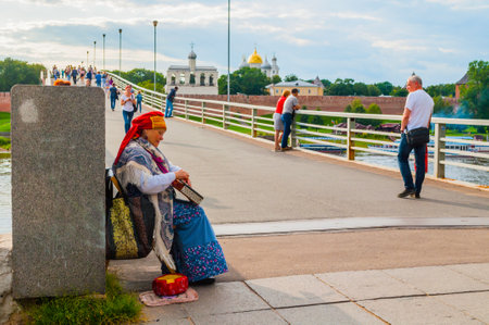 Veliky Novgorod,Russia -August 10, 2019. Woman dressed in Slavic folk clothes is playing the gusli - the oldest East Slavic multi-string plucked instrument. Kremlin fortress on the backgroundのeditorial素材