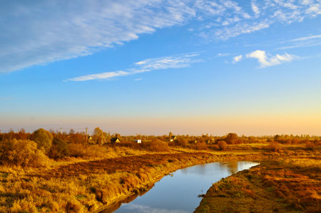 Autumn landscape. Small village at the bank of the river at the autumn evening in bright sunlight -...