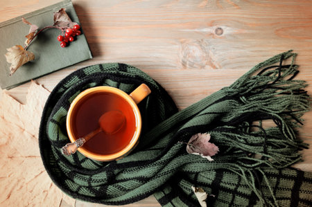 Autumn background. Cup of tea, old book and warm scarf on the wooden background. Autumn table at home, spending autumn at cozy homeの写真素材