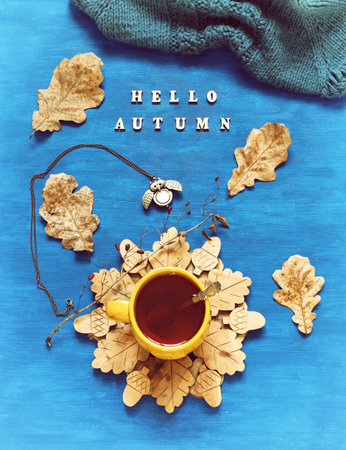 Autumn still life. Cup of tea with oak autumn leaves, warm scarf, metal clock and inscription Hello...