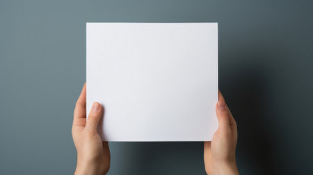 Female hands holding a blank white paper sheet on a gray background.の素材