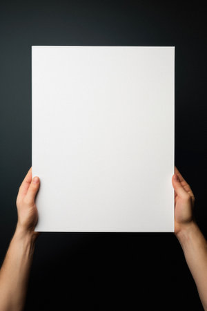 Hands holding blank paper on black background. Mockup for design.の素材