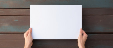 Hands holding white blank paper sheet on wooden table, top view.の素材