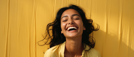 Happy Indian woman laughing and looking away on yellow background.の素材