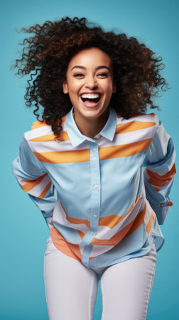 Excited african american woman in striped shirt smiling at camera isolated on blue.の素材