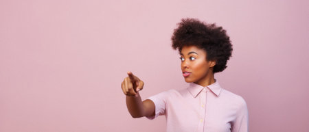 Young african american woman pointing at copy space on pink background.の素材