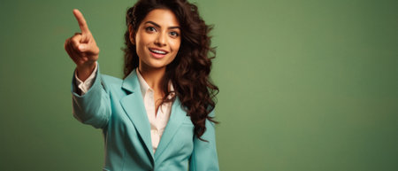 Smiling businesswoman in suit pointing with finger at empty space on green.の素材