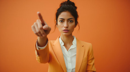 Serious businesswoman pointing with finger at camera isolated on orange background.の素材