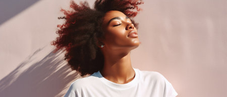 Young adult pretty African American woman model wearing white t-shirt with eyes closed on background. Face flawless fresh skin hair care cosmetic treatment makeup products skincare ad. Beauty portrait.の素材