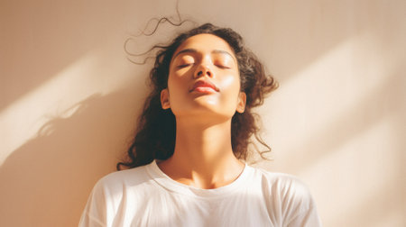 Young adult pretty Indian woman beauty model wearing white t-shirt posing with eyes closed on color background. Face flawless fresh skin hair care cosmetic treatment makeup products skincare ads.の素材