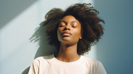 Young adult pretty African American woman model wearing white t-shirt with eyes closed on background. Face flawless fresh skin hair care cosmetic treatment makeup products skincare ad. Beauty portrait.の素材