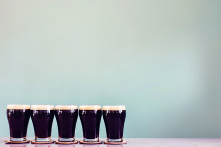 Glass pint of cold draft light lager or dark ale brewed beer with foam on table background. Brewery or pub bar advertising. Oktoberfest festival alcohol beverage or Saint Patricks day drink concept.の素材