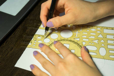 Girl with purple nails draws a circle with a ruler with figures