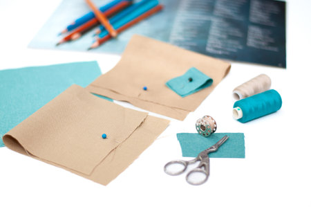 Samples of beige and turquoise fabric, scissors and coils with threads on a white background. Fabric...
