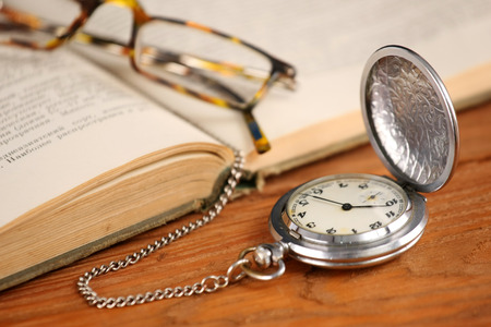 Vintage pocket watch glasses  and open old book on background of wooden planksの写真素材