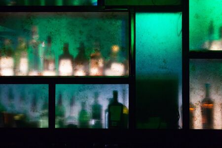 bar counter with bottles behind colored glass out of focusの写真素材