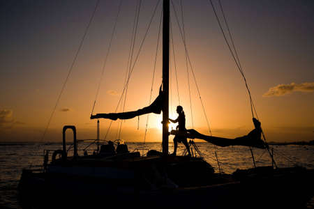 Silhouette of a man standing in his sailboat at sunset. Shot at Waikiki beach in Hololulu, Hawaii.の写真素材