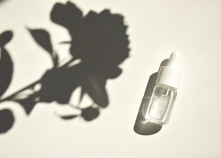 Aromatherapy oil, the concept of a natural cosmetic composition Flatley with a bottle of natural oil on a white background with contrasting shadows from flowers.の写真素材