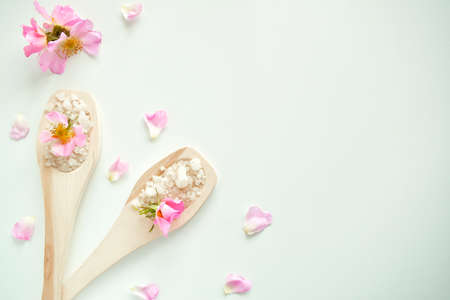 Bath salt in wooden spoons with flowers and rose petals, on a white background. The view from the top.の写真素材