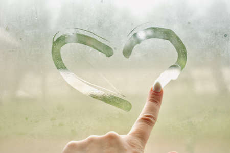 A hand on a Misty rainy window draws a heart, an abstract background. The view from the top. Copy spaceの写真素材