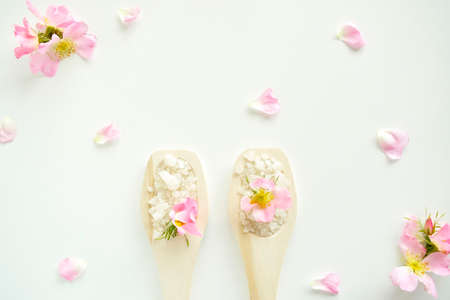 Bath salt in wooden spoons with flowers and rose petals, on a white background. Top view.の写真素材