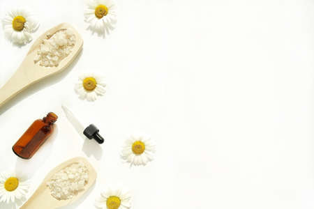 Bath salt in wooden spoons and a glass jar of cosmetic oil with chamomile, on a white background.の写真素材