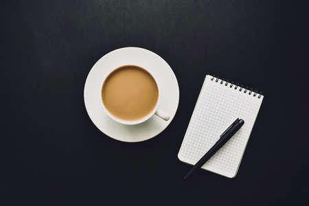 Cup of coffee with notebook and black pen on black background. Business planner.の写真素材