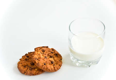 Oatmeal cookies with chocolate chips and a glass of milk on a white table.