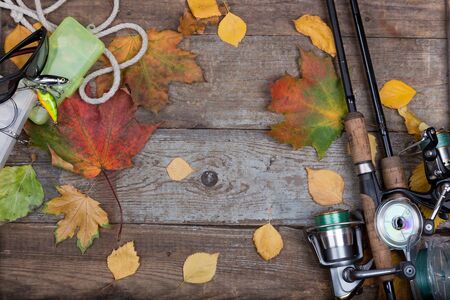 fishing tackles reel, line and lure on wooden board with leafs of autumnの写真素材