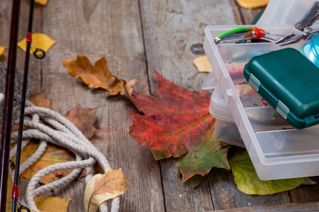 fishing tackles reel, line, wobbler, lure on wooden board with leafs of autumnの写真素材