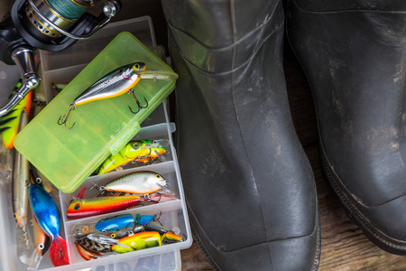 fishing tackles rod, reel, wobblers in boxes with rubber boots on timber board background. for design advertising or publicationの写真素材