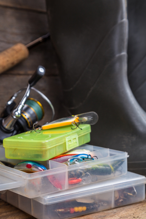 fishing tackles rod, reel, wobblers in boxes with rubber boots on timber board background. for design advertising or publicationの写真素材