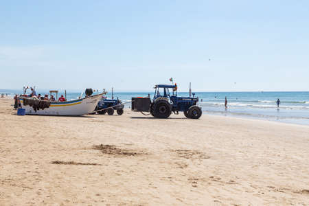 Costa da Caparica, Portugal - September 10, 2020: An artel of fishermen trawls fish from the tourist beach using a tractors. Vacationers watch and help.のeditorial素材