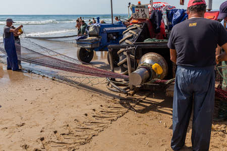 Costa da Caparica, Portugal - September 10, 2020: An artel of fishermen trawls fish from the tourist beach using a tractors. Vacationers watch and help.のeditorial素材