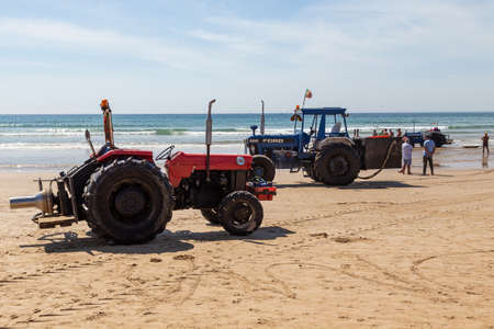 Costa da Caparica, Portugal - September 10, 2020: An artel of fishermen trawls fish from the tourist beach using a tractors. Vacationers watch and help.のeditorial素材