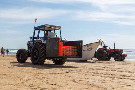 Costa da Caparica, Portugal - September 10, 2020: An artel of fishermen trawls fish from the tourist beach using a tractors. Vacationers watch and help.のeditorial素材