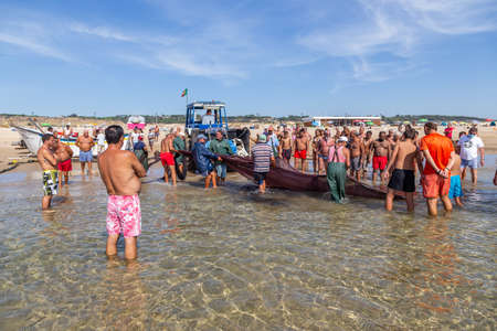 Costa da Caparica, Portugal - September 10, 2020: An artel of fishermen trawls fish from the tourist beach using a tractors. Vacationers watch and help.のeditorial素材